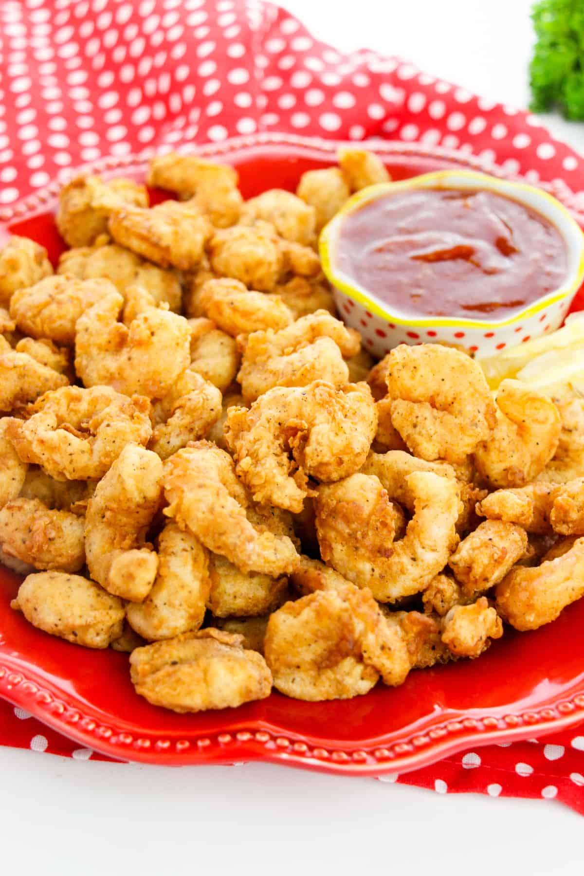 Popcorn shrimp with cup of cocktail sauce on red plate with red cloth napkin in the background