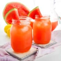Two watermelon lemonades served in mason jars with watermelon wedges on the rim