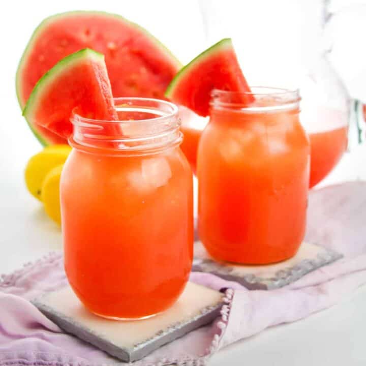 Two watermelon lemonades served in mason jars with watermelon wedges on the rim