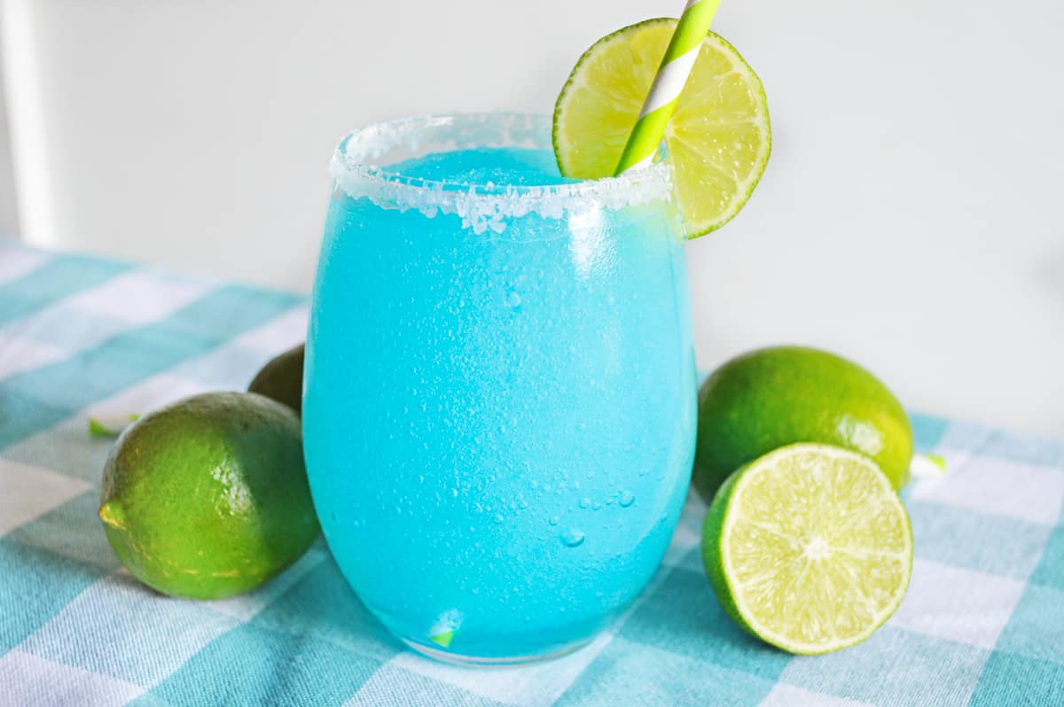 Blue lagoon margarita served in stemless glass rimmed with sugar and garnished with a slice of lime.