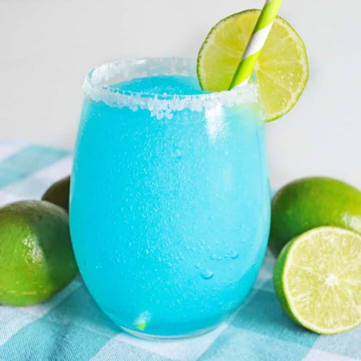 Blue lagoon margarita served in stemless glass rimmed with sugar and garnished with a slice of lime.