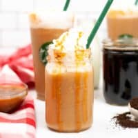 Caramel Frappuccino topped with whipped cream and caramel drizzle served in a mason jar with green straw