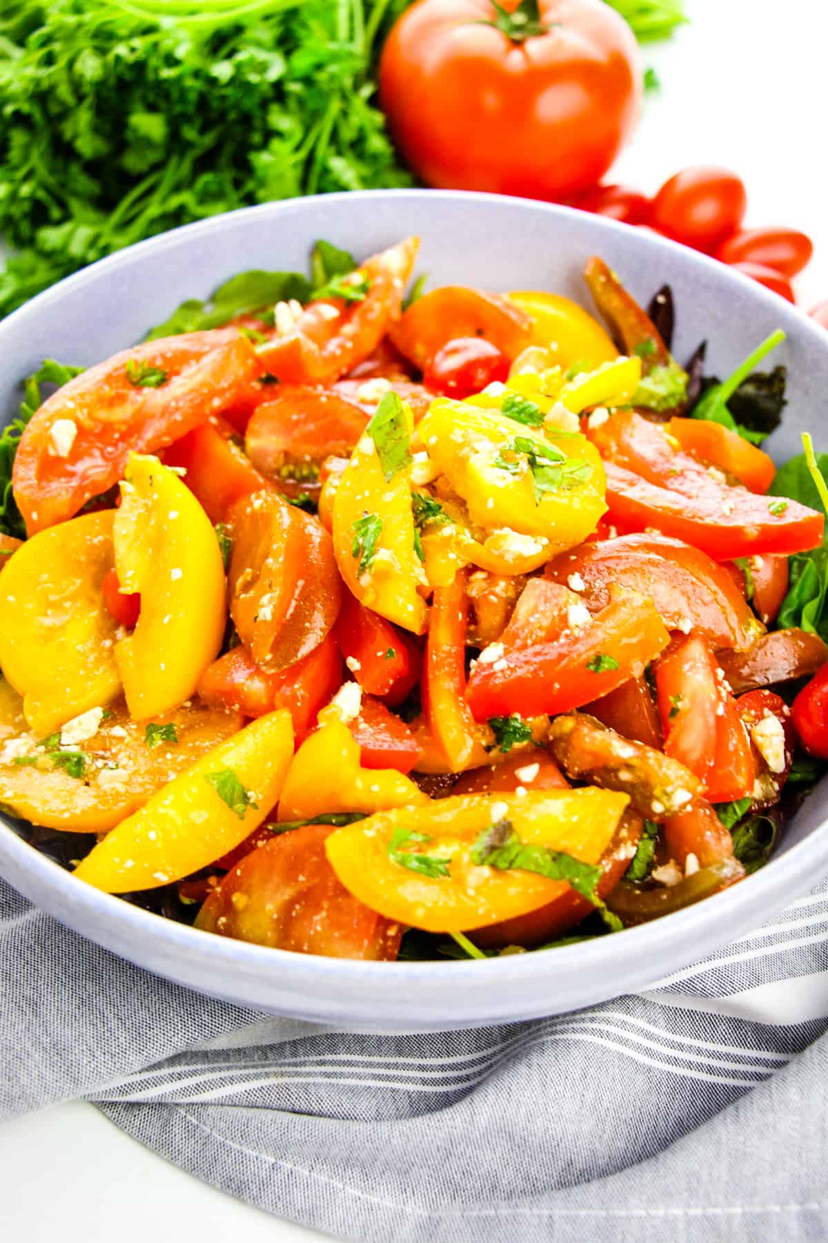 Heirloom Tomato Salad served in large grey bowl on bed of lettuce with parsley and tomatoes in background