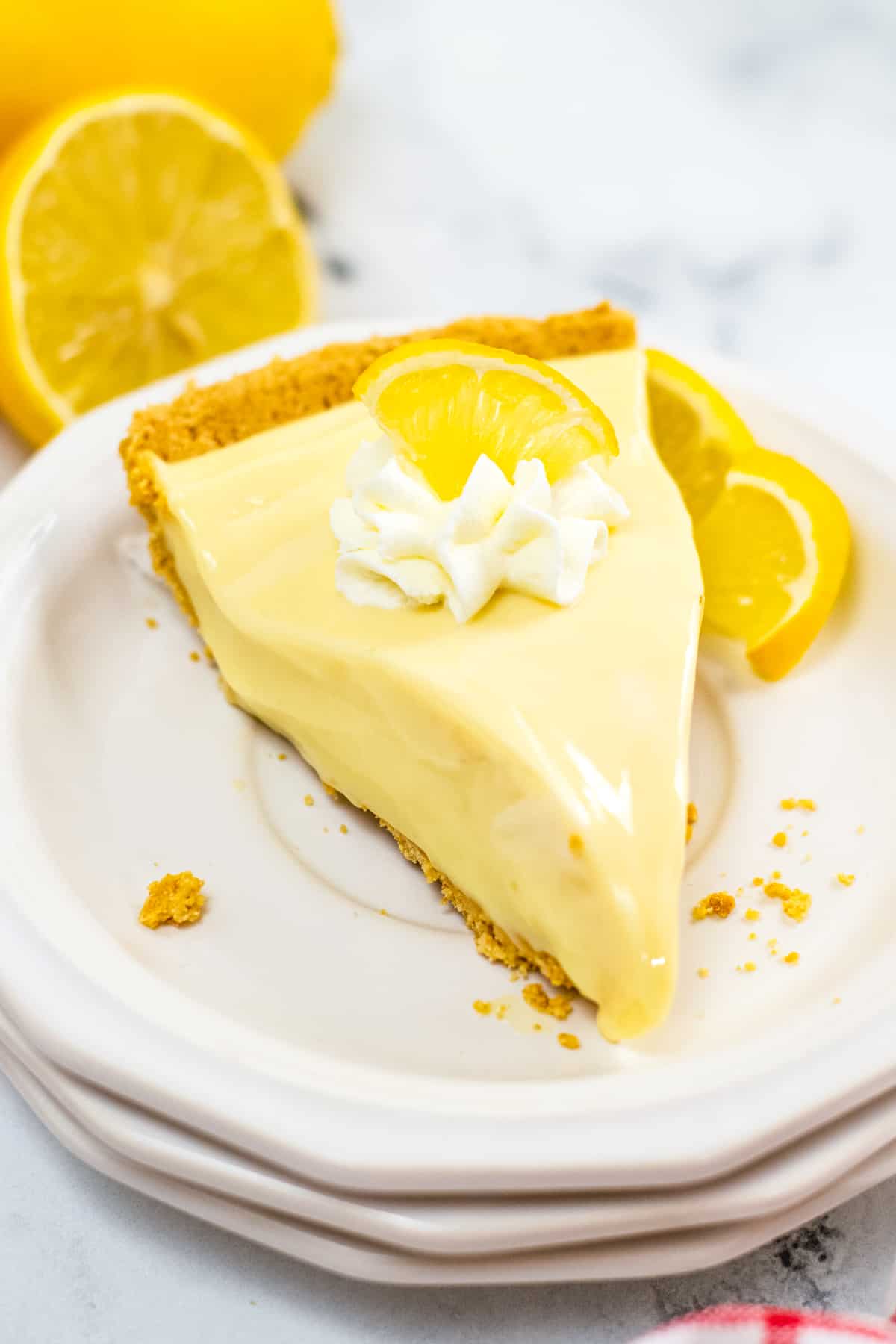 Piece of no bake lemon pie with graham cracker crust and topped with lemon slice and whipped cream