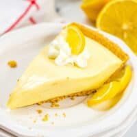 Lemon Icebox Pie slice on white plate, topped with whipped cream and lemon slice
