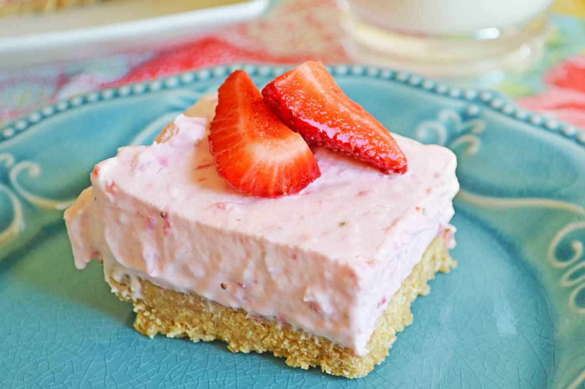 No-Bake Strawberry Cheesecake Bar with a thick graham cracker crust on blue plate topped with fresh strawberries