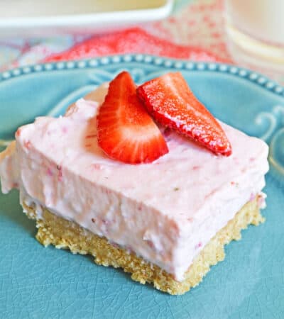 No-Bake Strawberry Cheesecake Bar with a thick graham cracker crust on blue plate topped with fresh strawberries