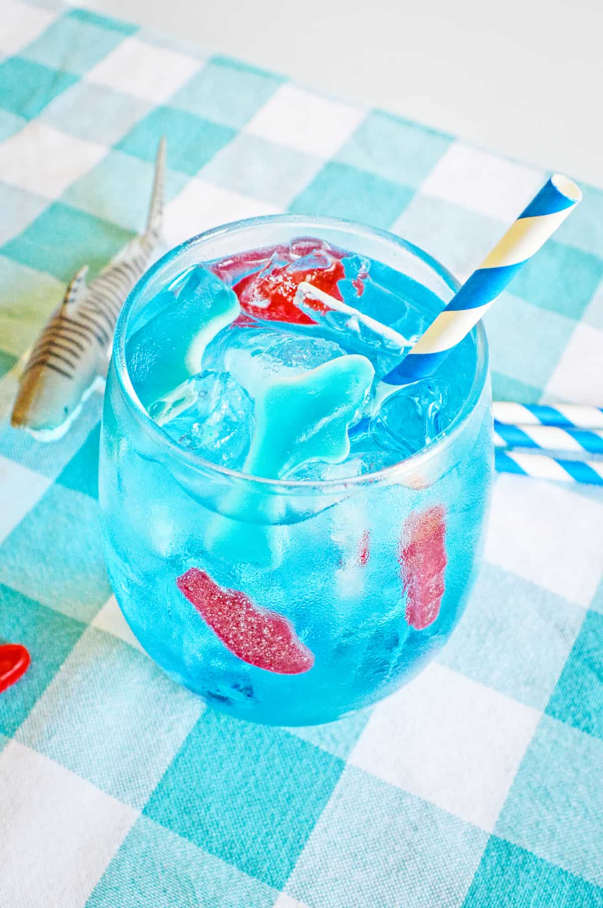 Homemade version of Sonic's ocean water drink in a glass with ice, swedish fish, gummy shark, and blue and white paper straw