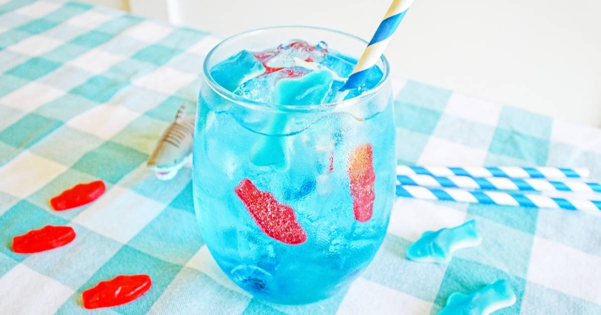 bright blue drink in stemless wine glass with ice, swedish fish, and blue paper straw