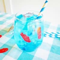 Blue ocean water drink in glass with ice, gummy fish, gummy shark, and blue and white paper straw