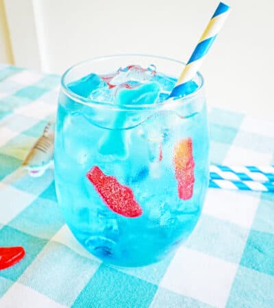Blue ocean water drink in glass with ice, gummy fish, gummy shark, and blue and white paper straw