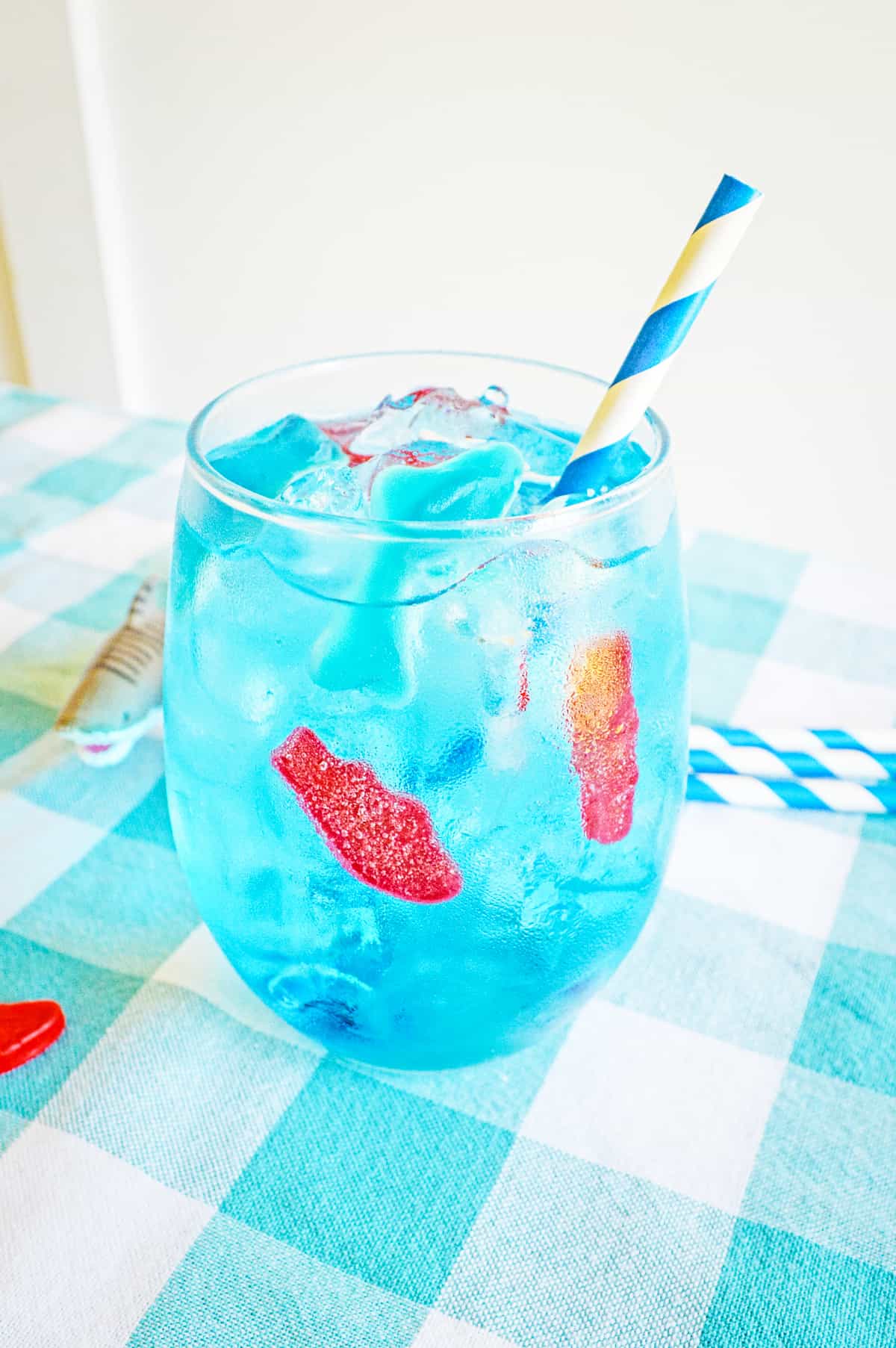 Blue ocean water drink in glass with ice, gummy fish, gummy shark, and blue and white paper straw