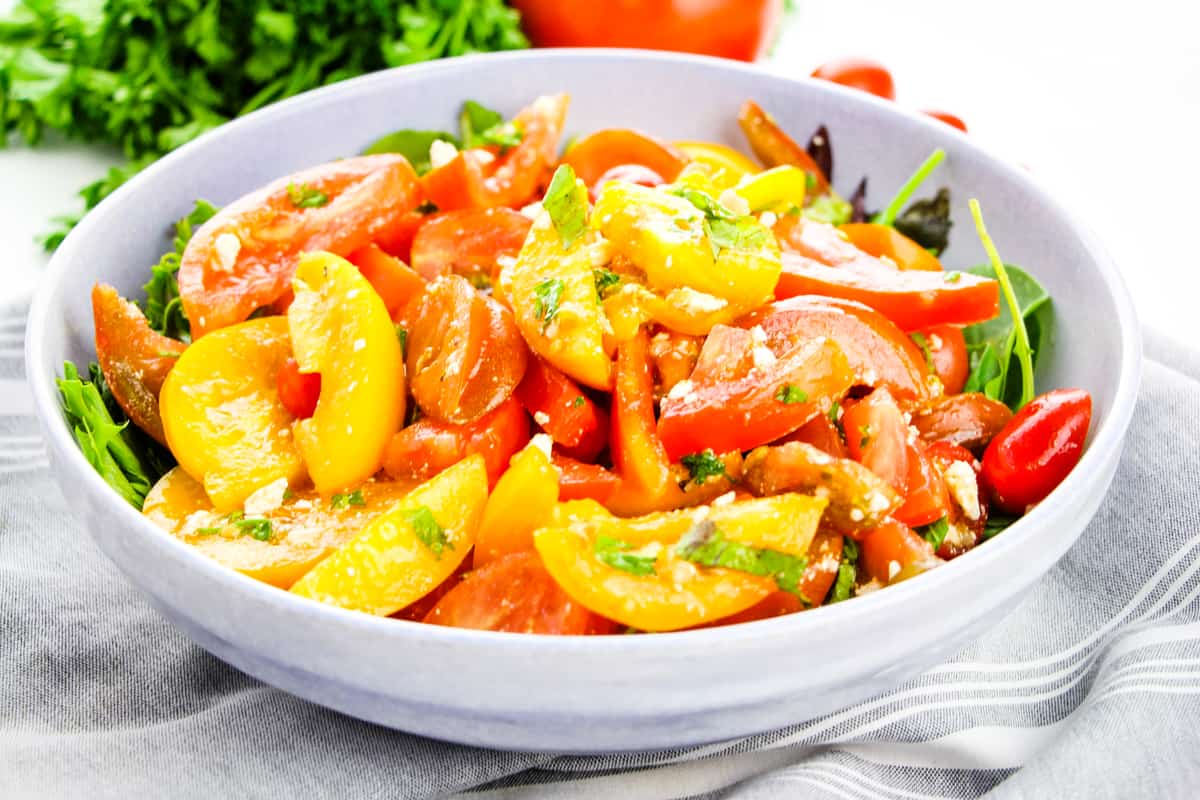 Colored tomato salad with crumbled feta and vinaigrette dressing served on bed of lettuce