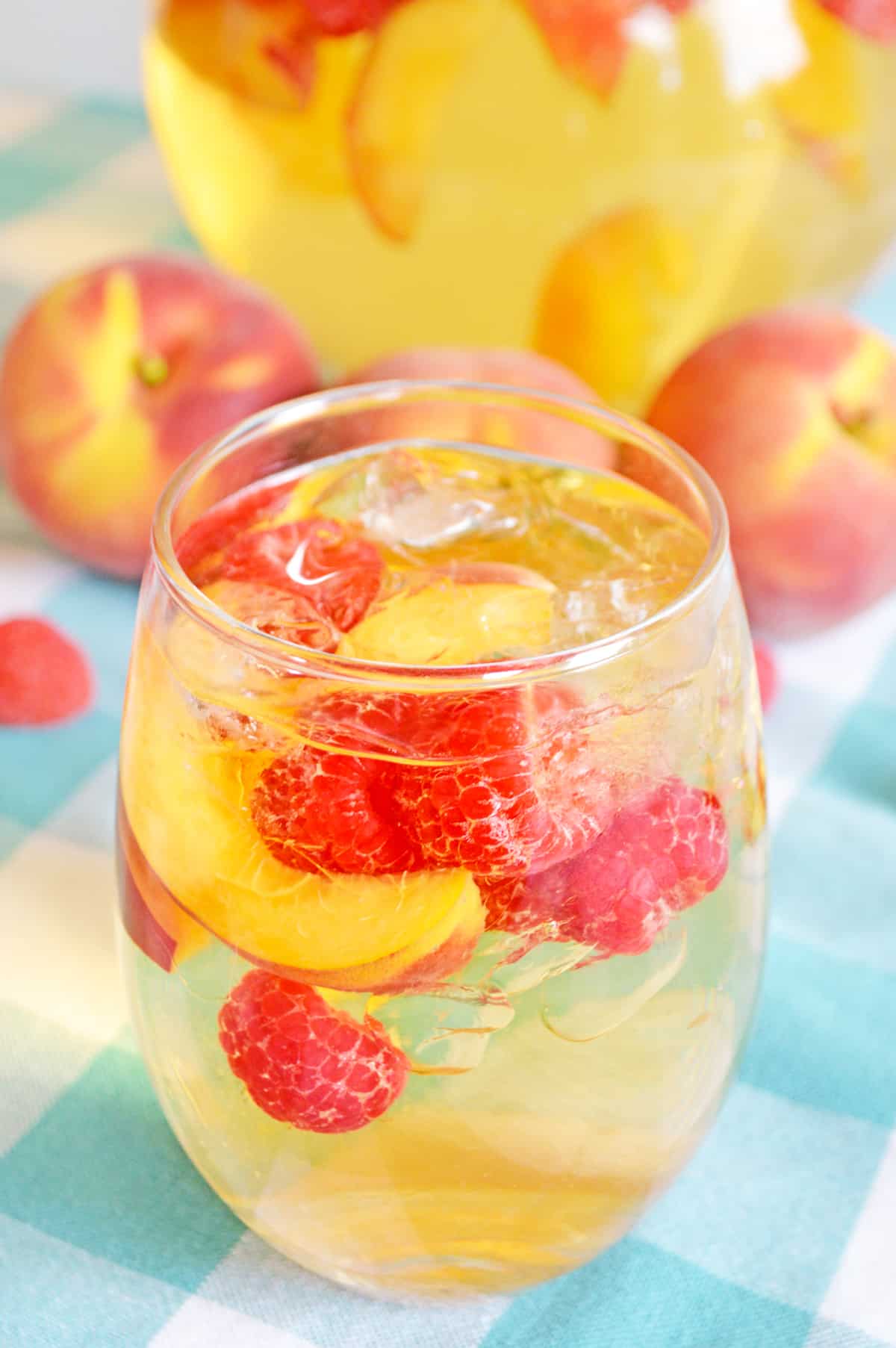 White sangria with peaches and raspberries in wine glass with pitcher and fresh fruit in background