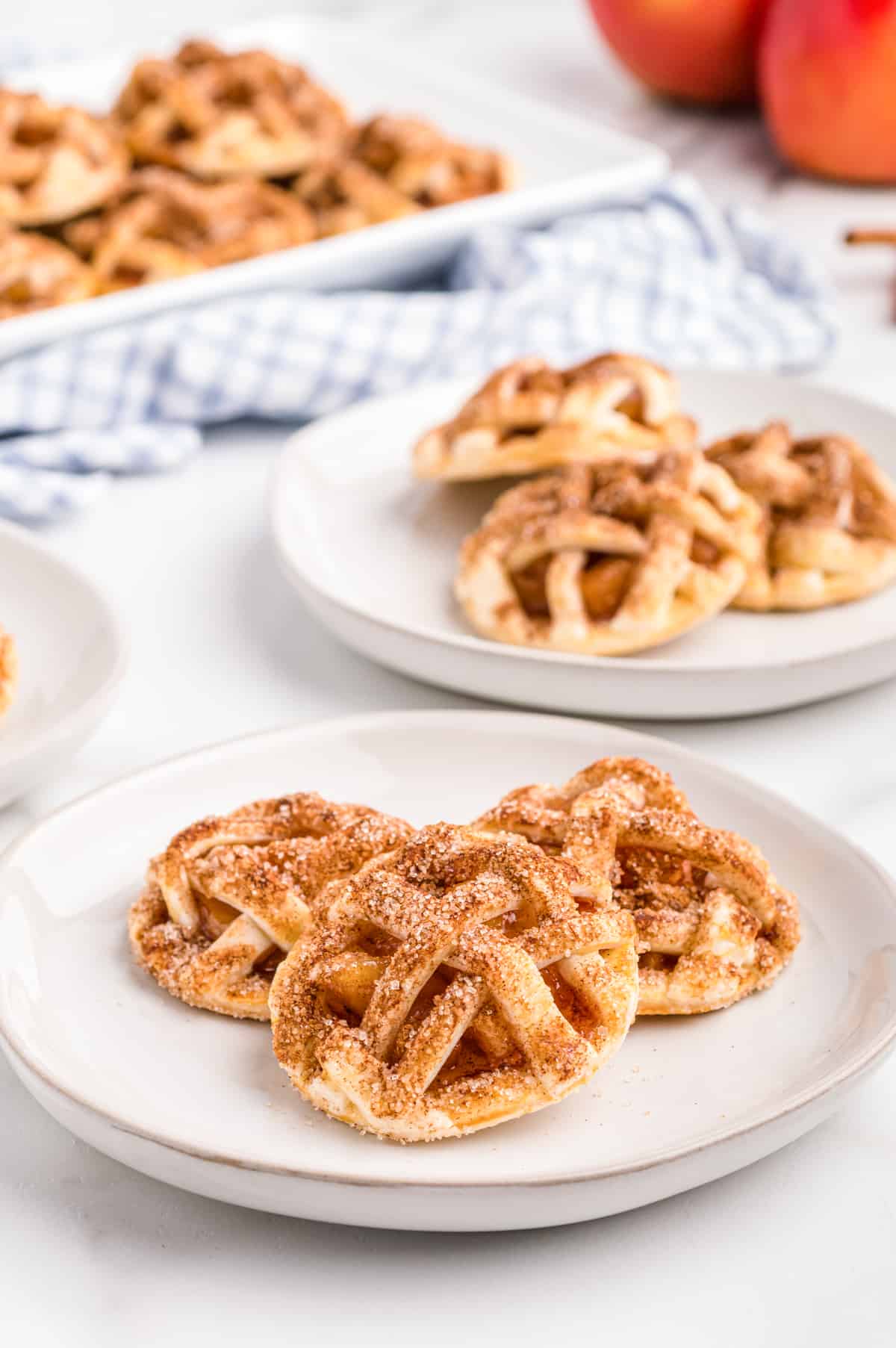 Apple pie cookies on white plates with cloth napkin and red apples in background