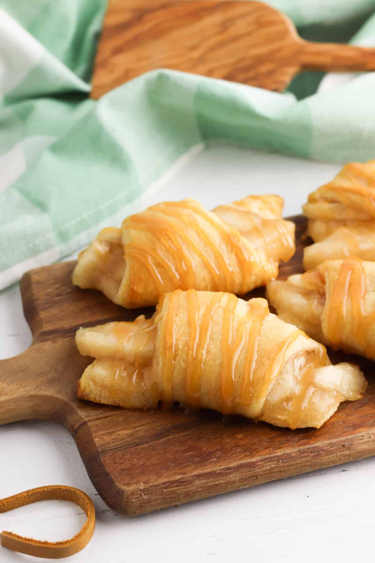 Crescent rolls filled with apple pie filling and drizzles with caramel sauce on wooden cutting board