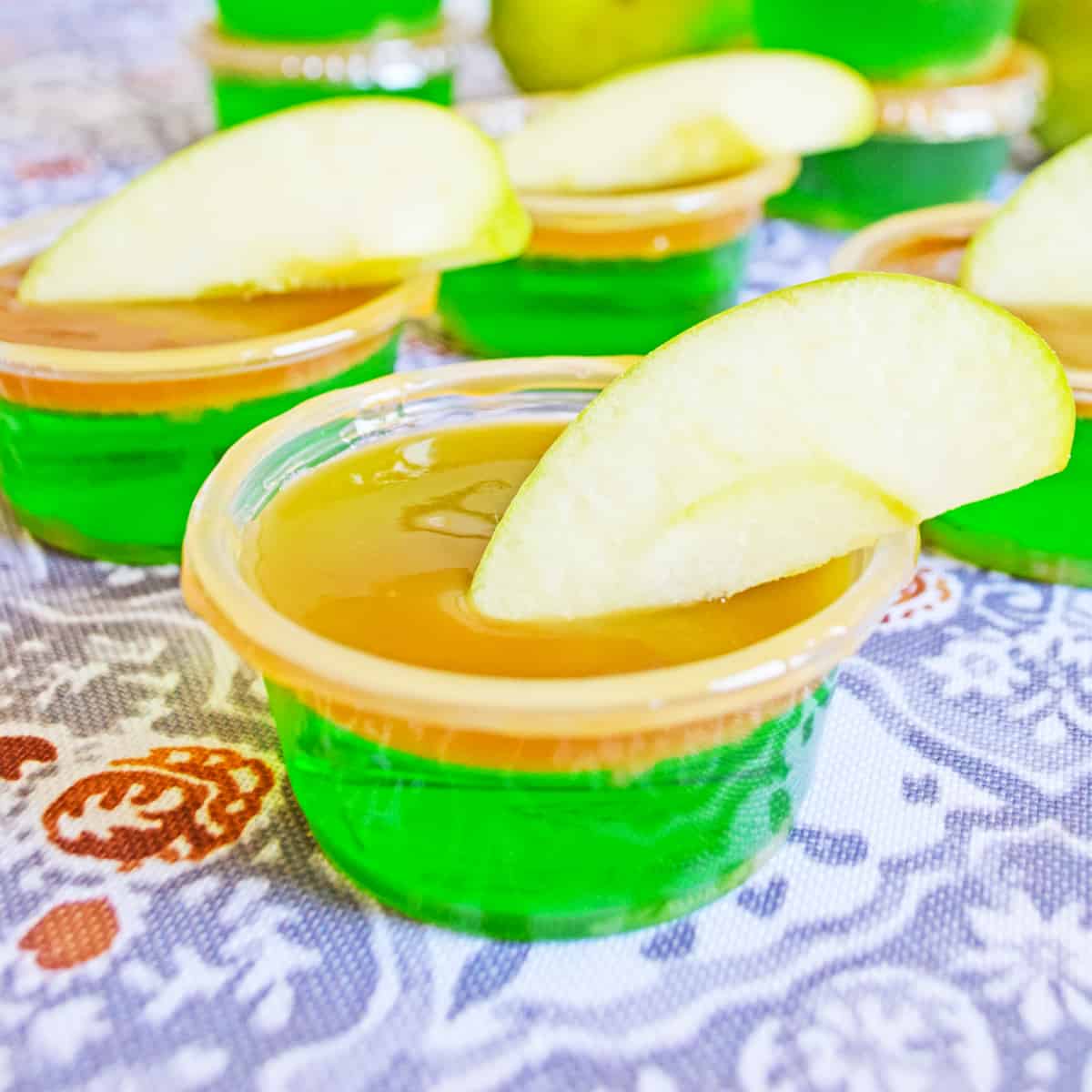 Green apple jello shot with caramel vodka, caramel topping, and fresh apple wedge.