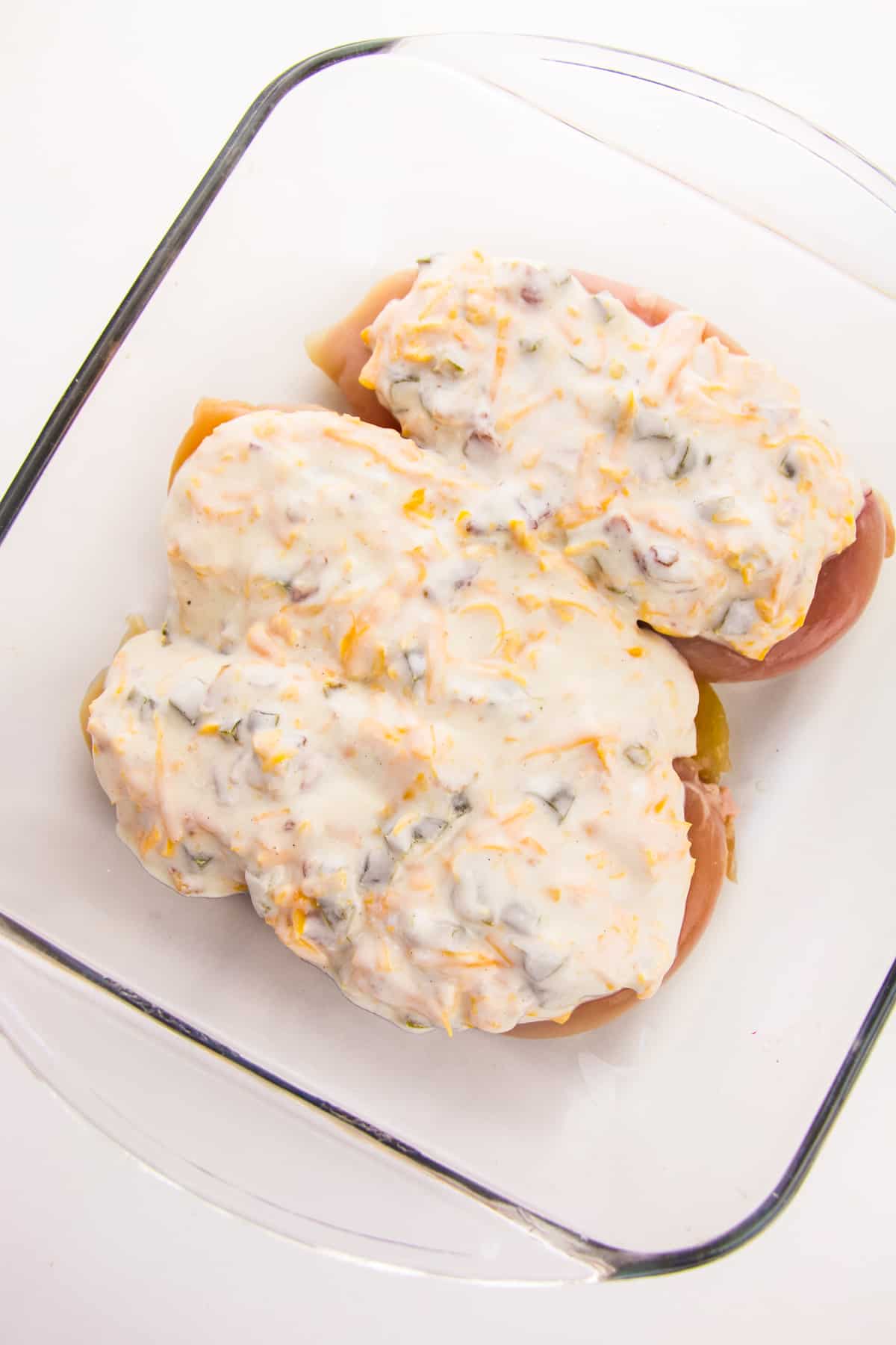 Chicken breasts topped with creamy jalapeno mixture in glass baking dish