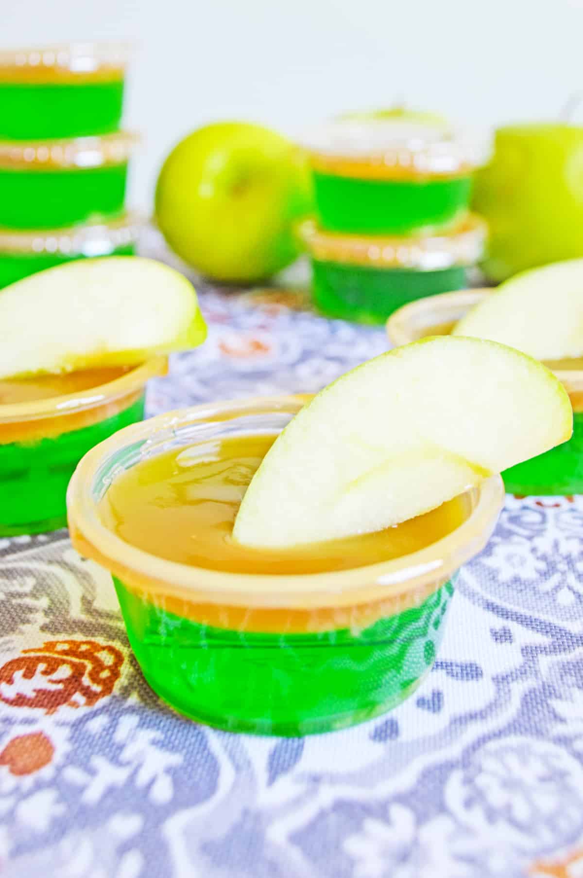 Caramel Apple Jello Shot in plastic shot glass with caramel topping and garnished with apple wedge.