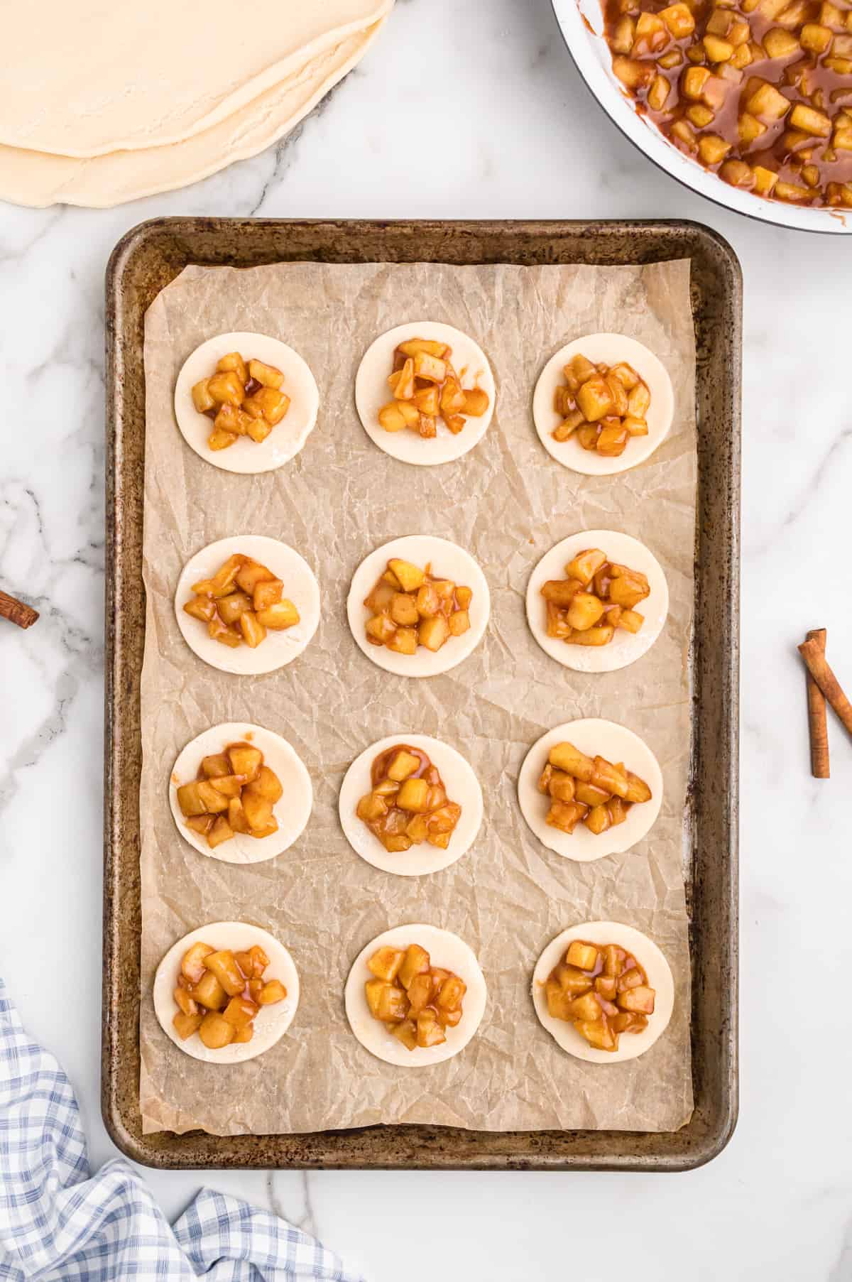 parchment lined baking sheet with 12 pie crust circles topped with apple pie filling