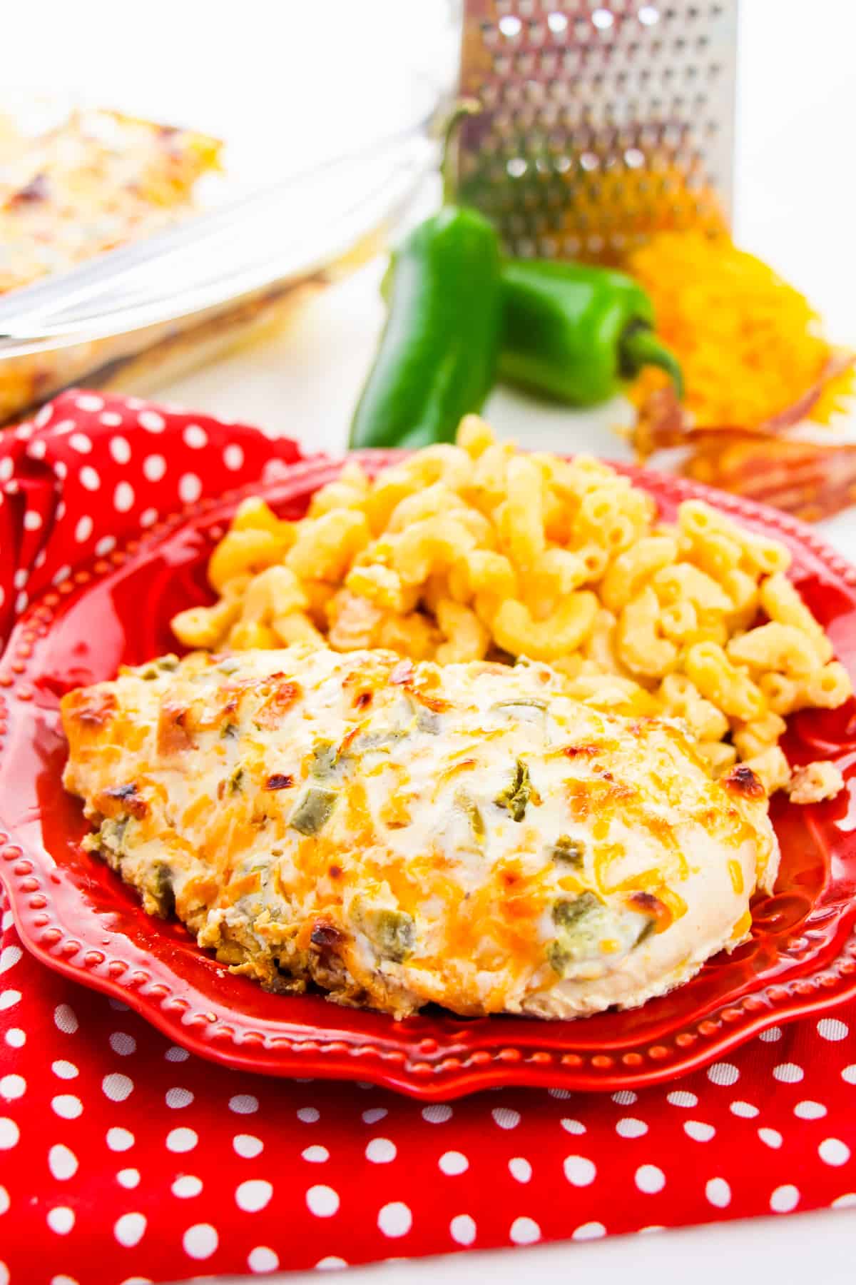 jalapeño popper chicken breast plated with side of macaroni and cheese. fresh jalapeno peppers and shredded cheese are in background