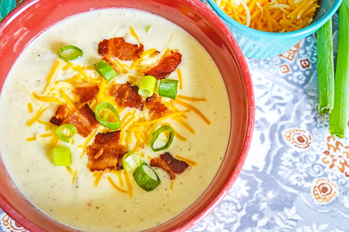 top down view of bowl of crockpot loaded baked potato soup topped with bacon, green onions, and cheese