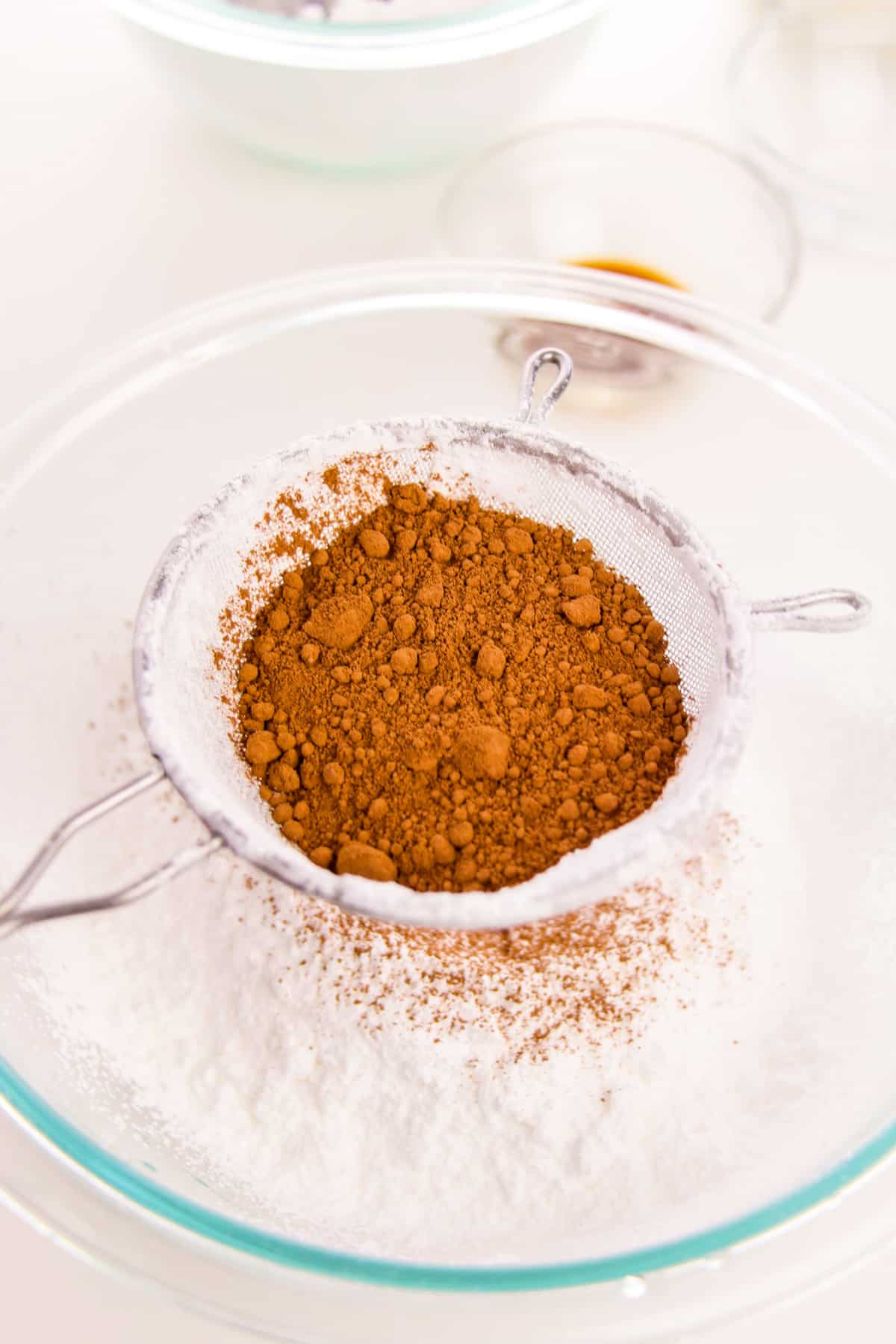 Cocoa powder being sifted into glass bowl of powdered sugar