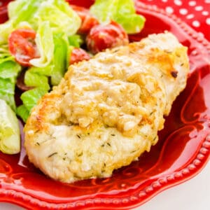 Smothered Chicken Breast served with salad on a red plate.