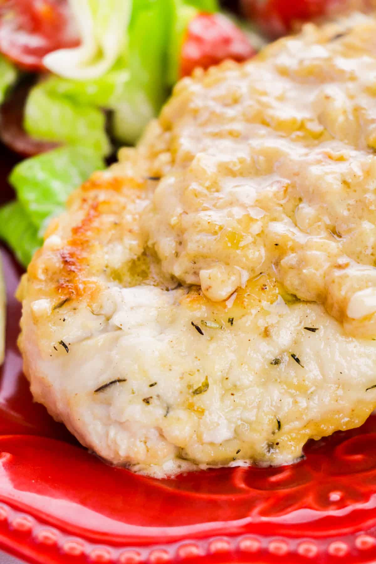 Smothered Chicken Breast served with salad on a red plate.