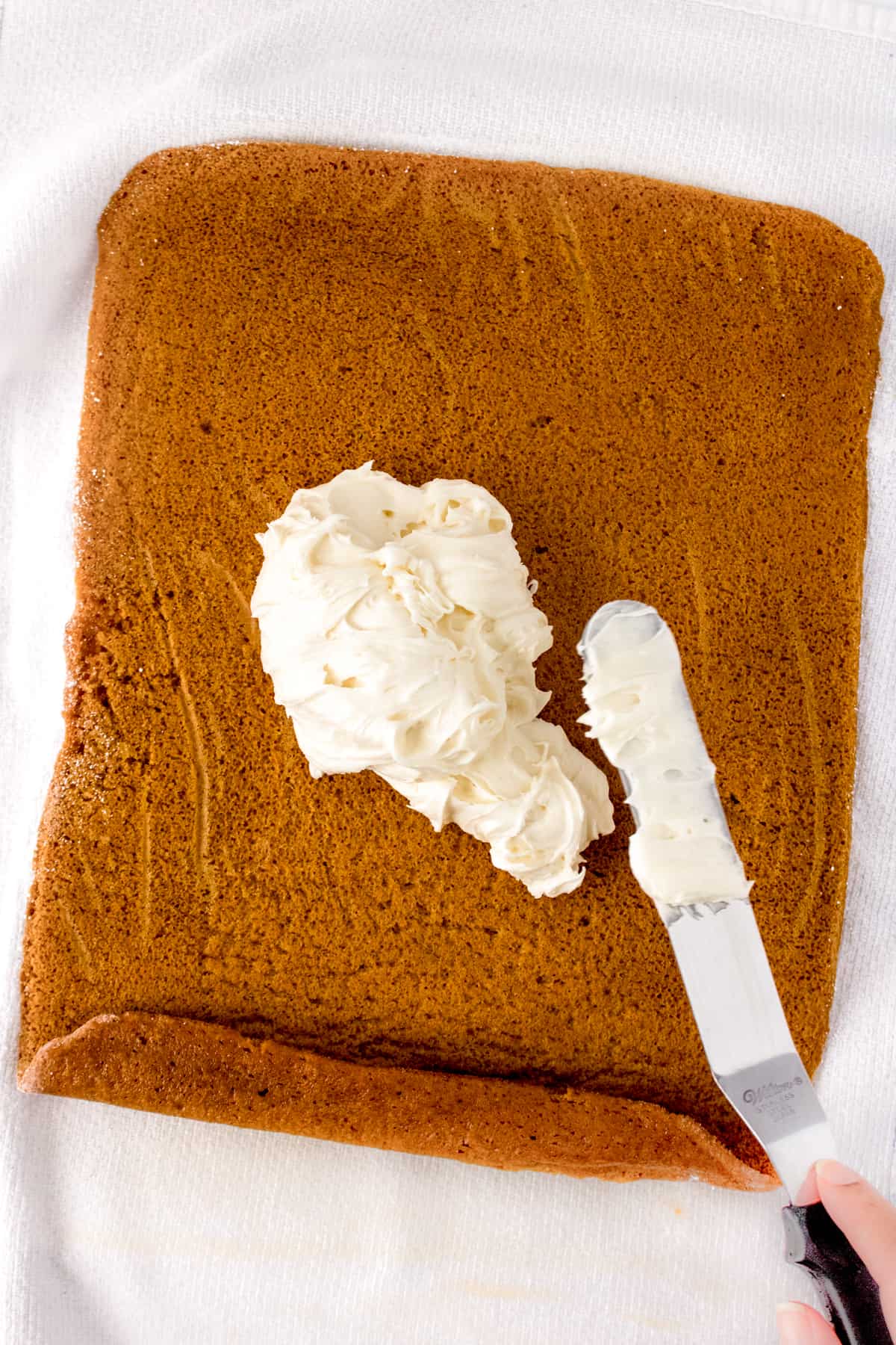 Cream cheese frosting being spread with an offset spatula on pumpkin roll cake