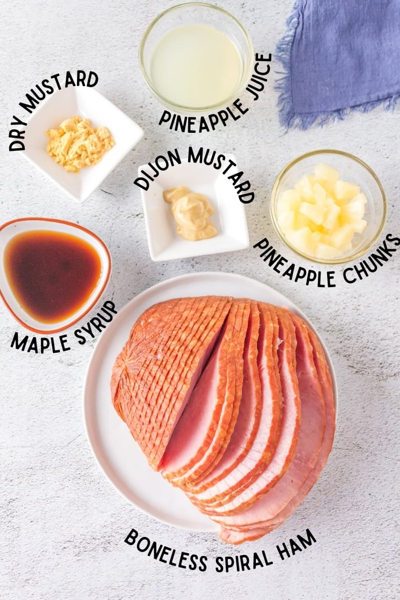 Top-down view of ingredients on countertop: dry mustard, pineapple juice, pineapple chunks, dijon mustard, maple syrup, and boneless spiral cut ham