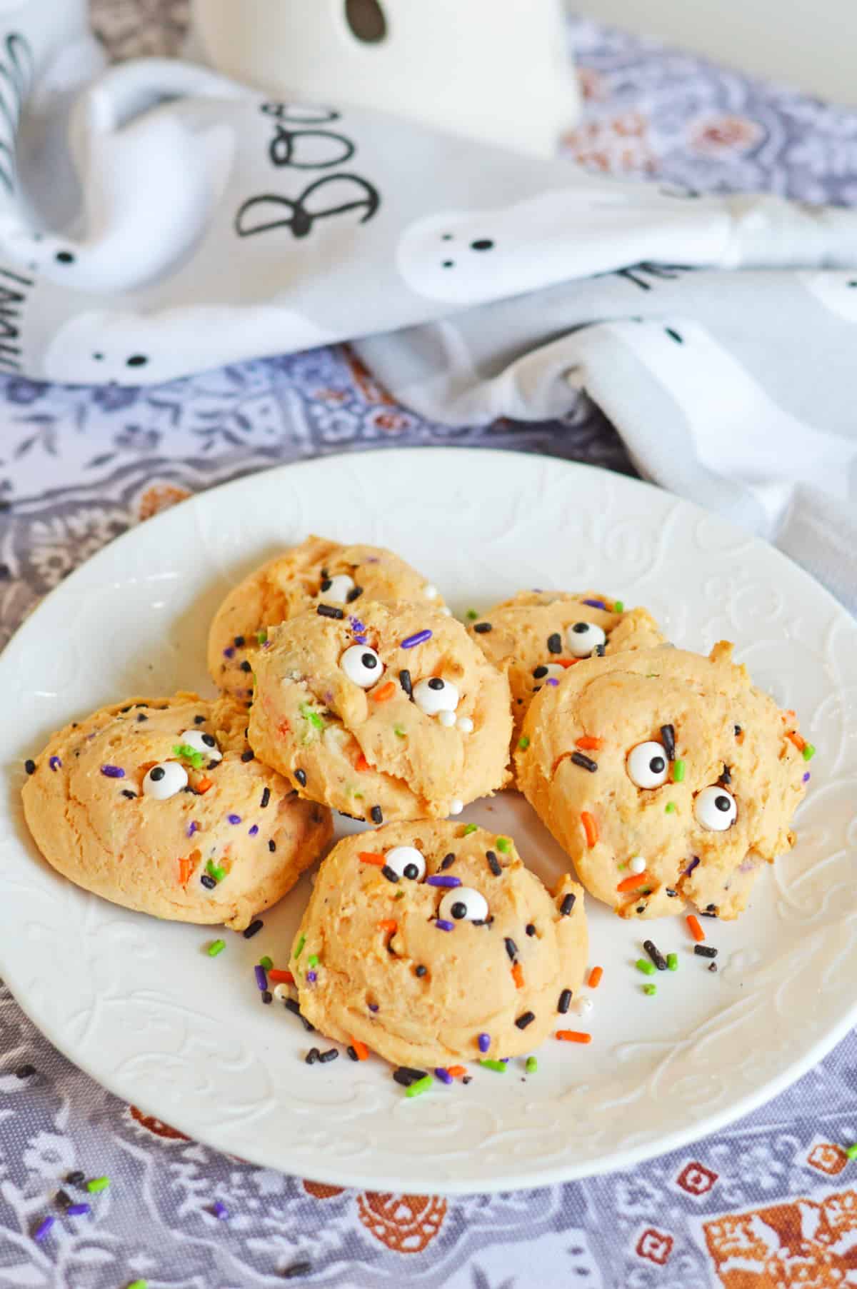 Orange Halloween cookies with sprinkles and eyeballs on a white plate