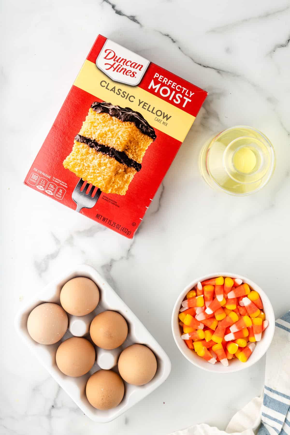 Box of Duncan Hines Perfectly Moist Classic Yellow Cake Mix, bottle of oil, 6 eggs in white carton, bowl of candy corn