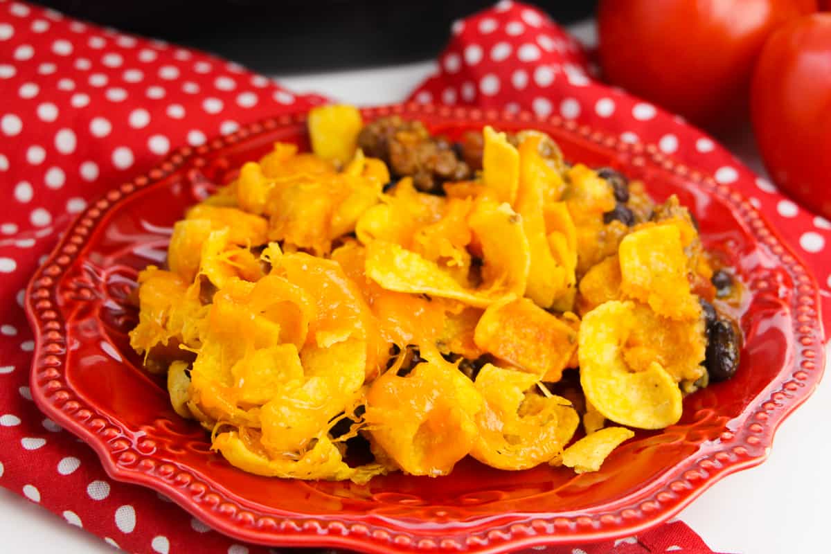 Crockpot Frito Casserole on red plate with red napkin and tomatoes in background