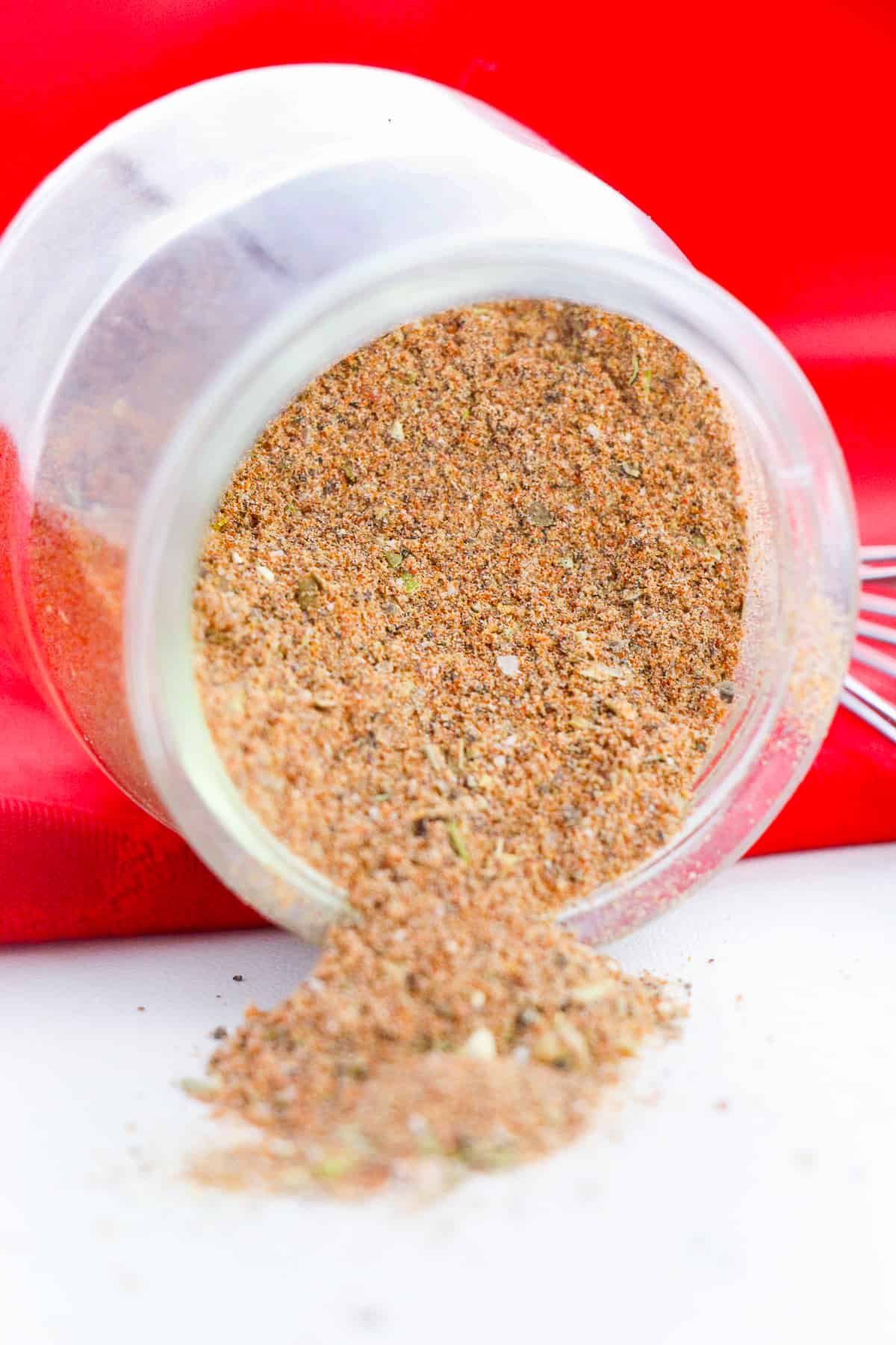 Jar of homemade chili seasoning mix laying down on its side with the seasoning falling out onto tabletop