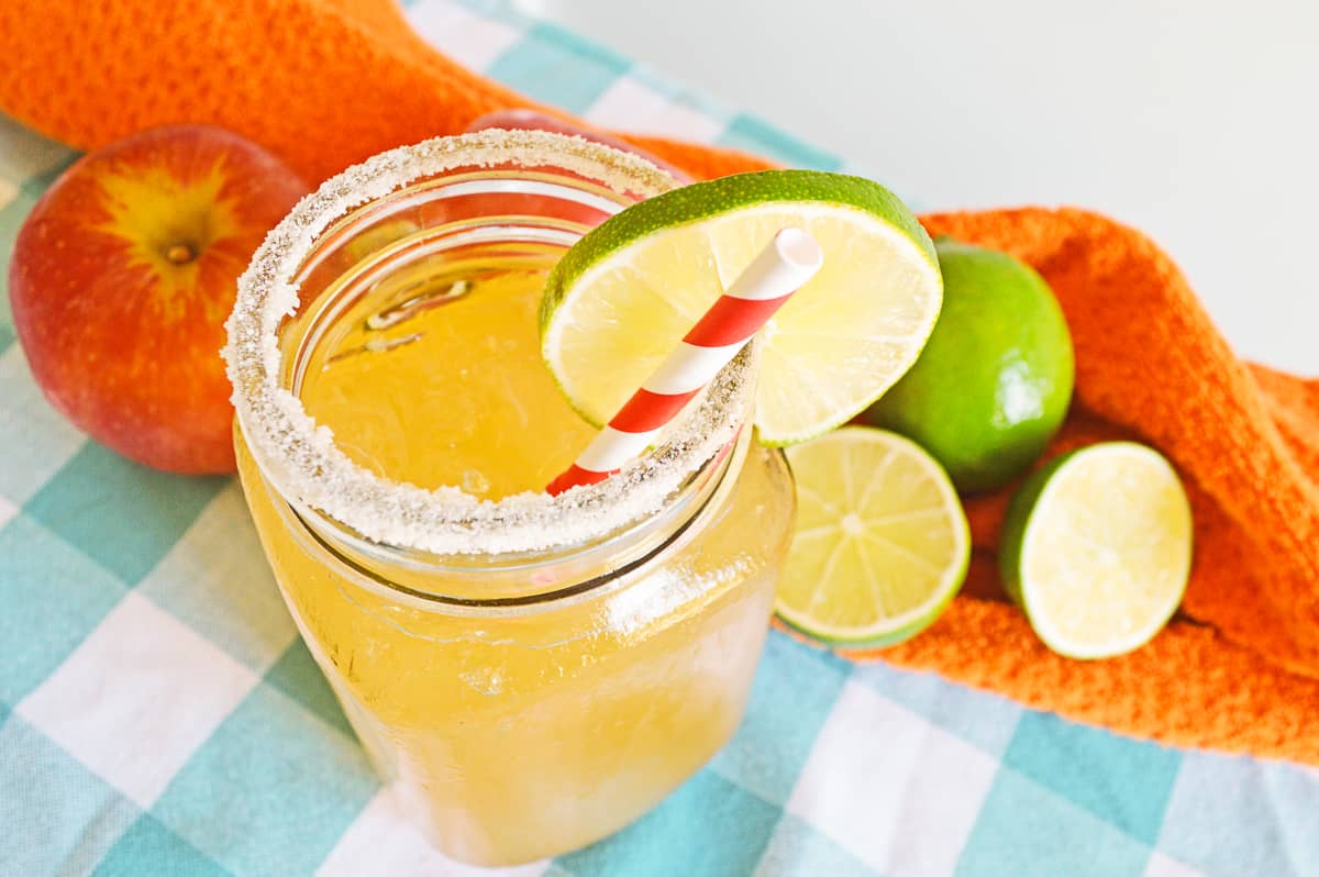 Top down view of yellow-ish orange-ish margarita in glass mason jar rimmed with sugar and garnished with lime