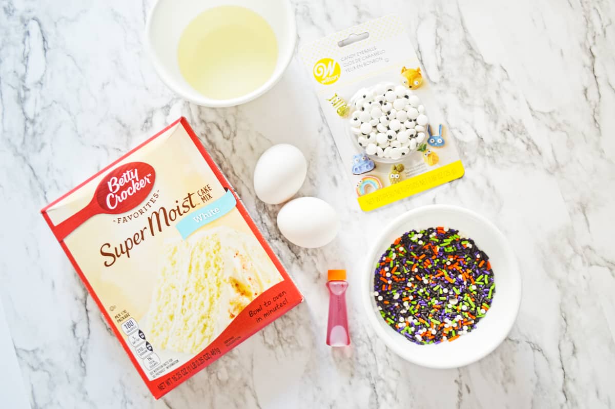 Box of white cake mix, oil, 2 eggs, candy eyes, Halloween sprinkles, and orange food coloring