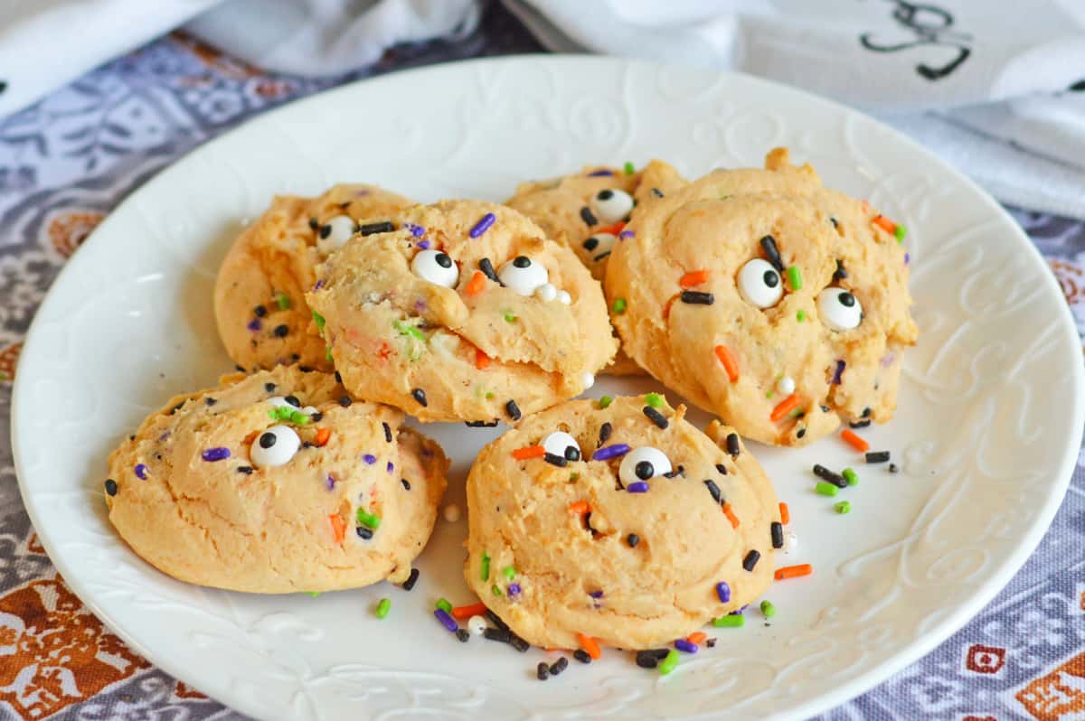 Orange cake mix cookies with Halloween sprinkles and eyeballs piled on a white plate