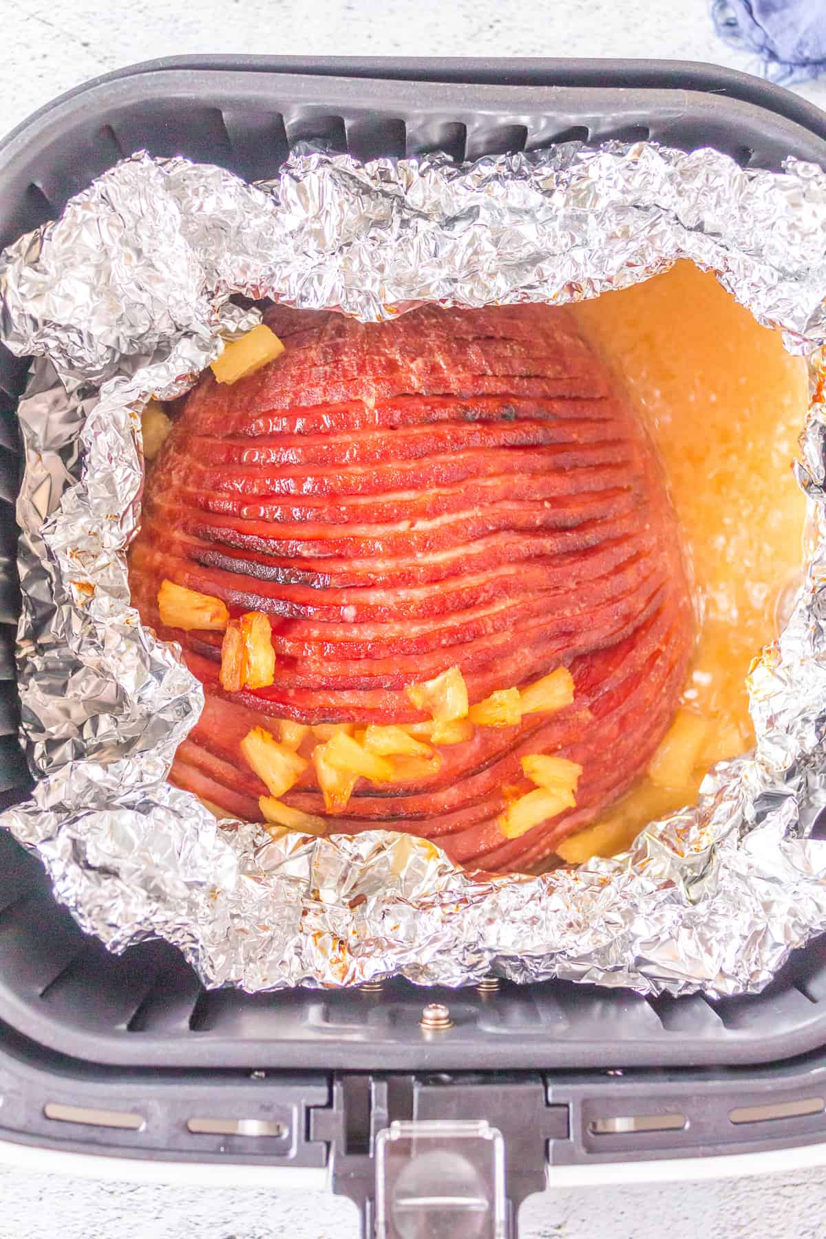 Glazed ham in air fryer basket with foil pulled back, top browned, and pineapples cooked.