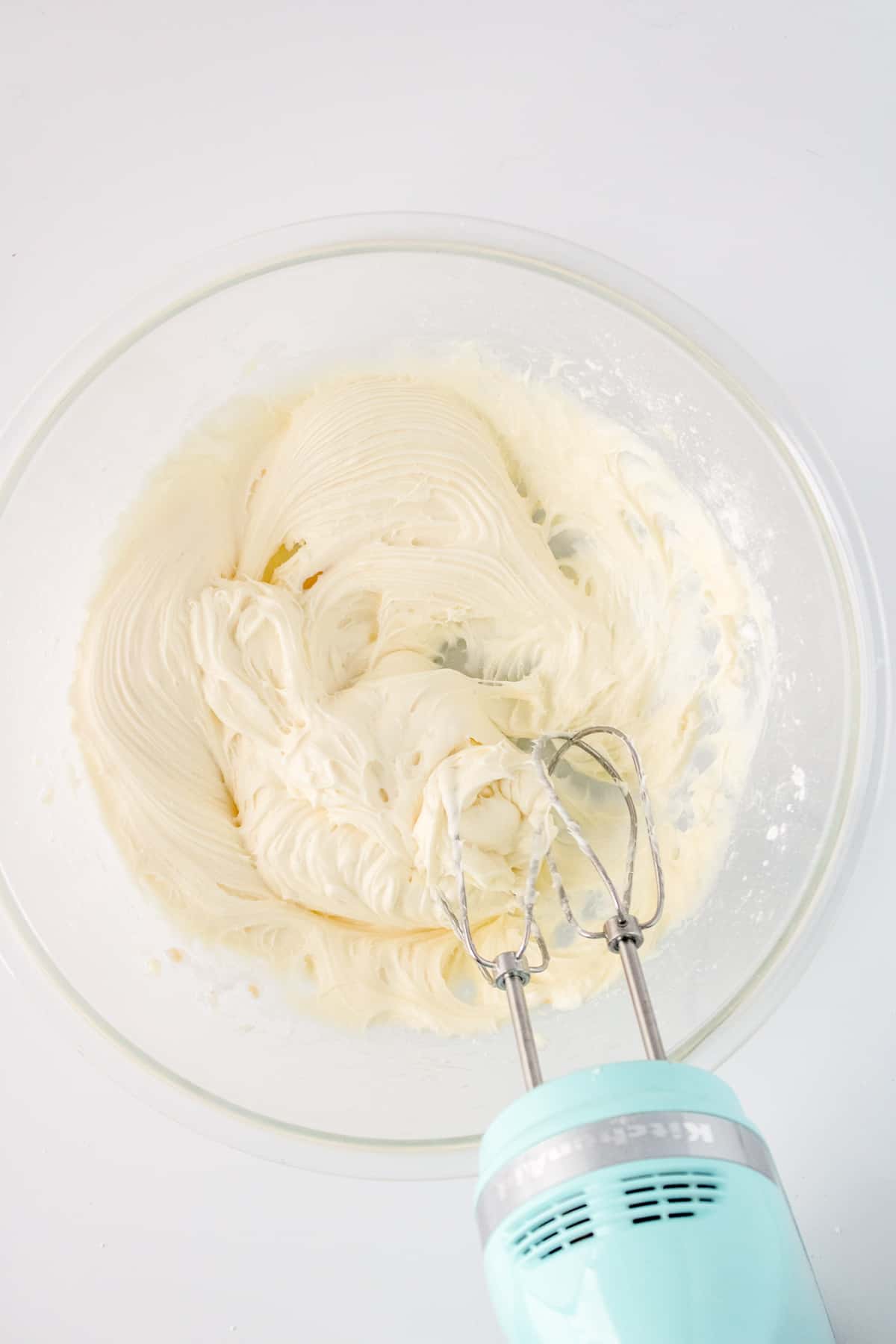 cream cheese filling being whipped in glass bowl with a hand mixer