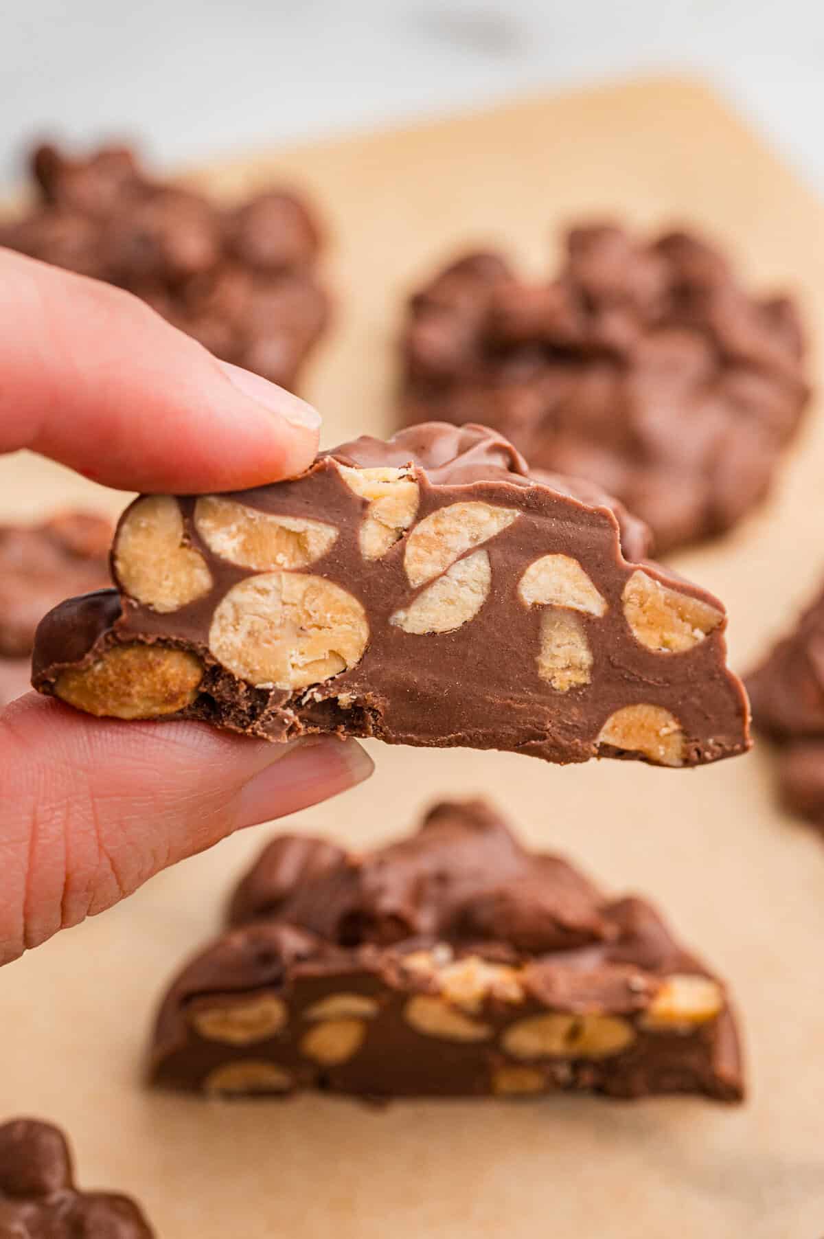 Close-up of a hand holding a piece of crock pot christmas candy with visible peanuts inside.