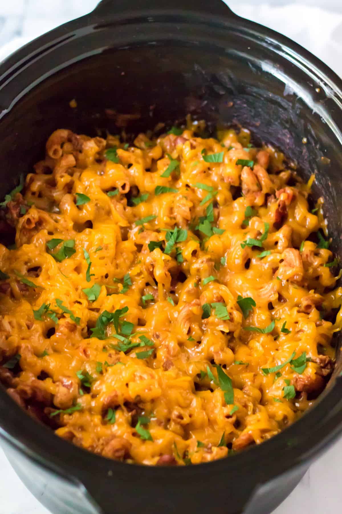 Slow Cooker chili mac with cheese, beans, and garnished with chopped parsley.