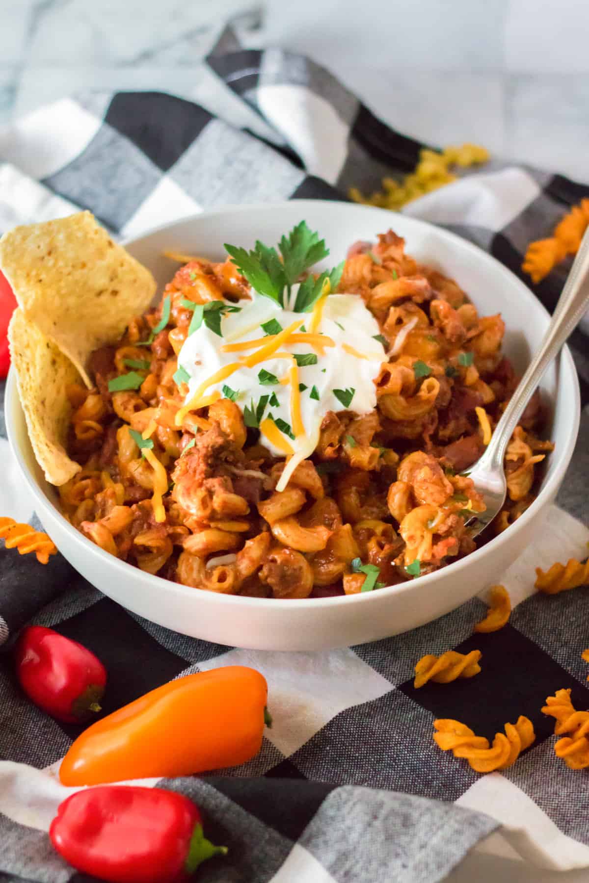 Slow cooker chili mac in a bowl topped with sour cream, shredded cheese, parsley, and tortilla chips.