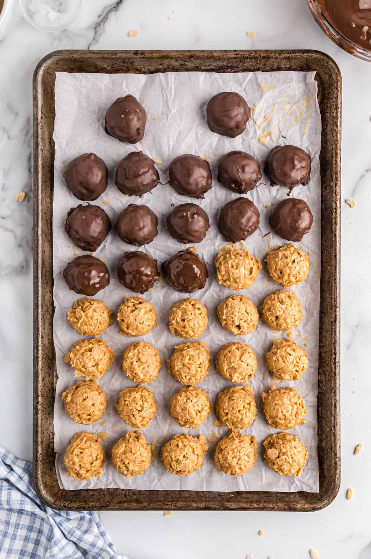 Crispy peanut butter balls on lined baking sheet, half are coated with melted chocolate