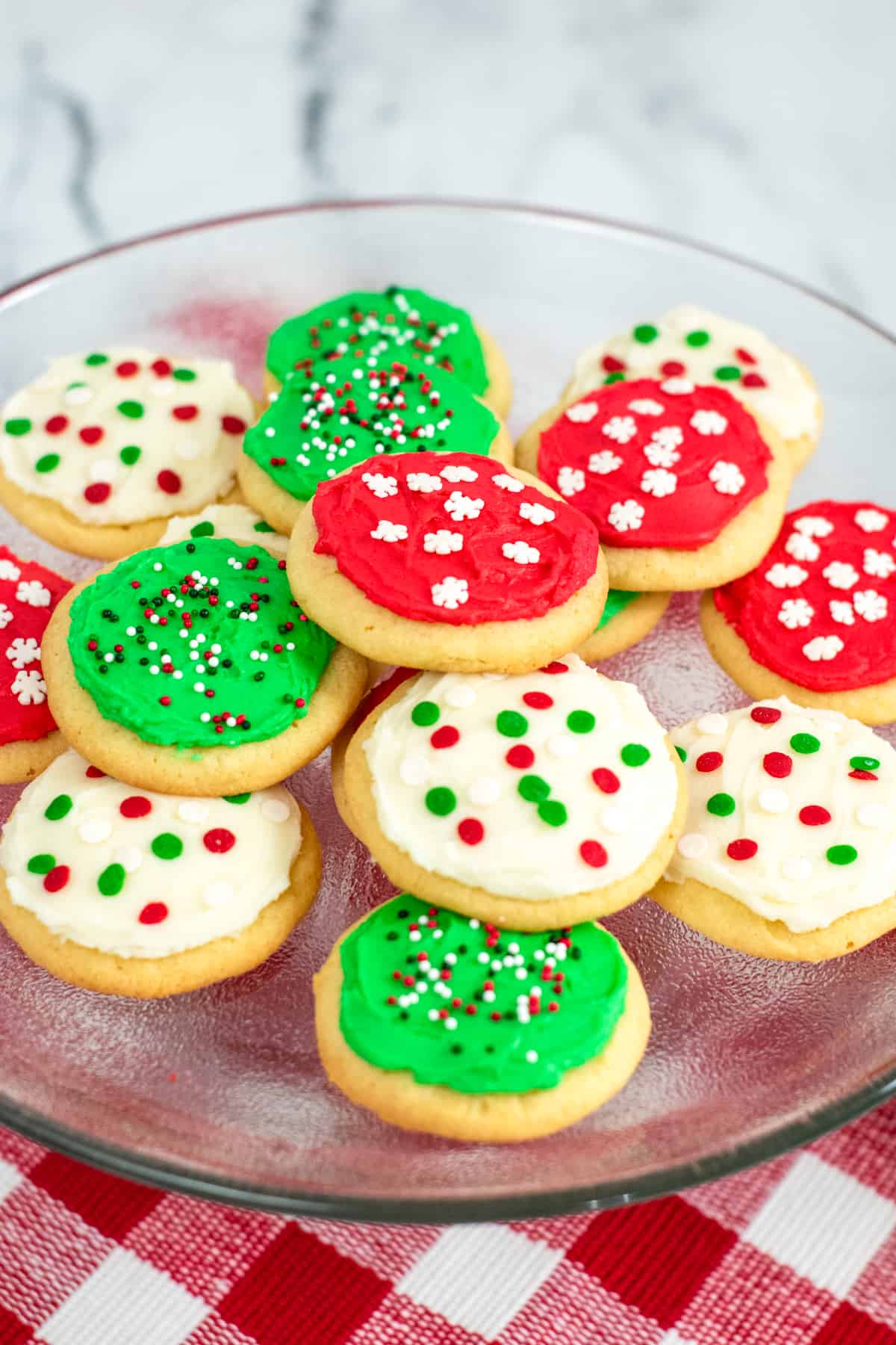 Platter of round frosted sugar cookies decorated with red, green, and white frosting and christmas sprinkles