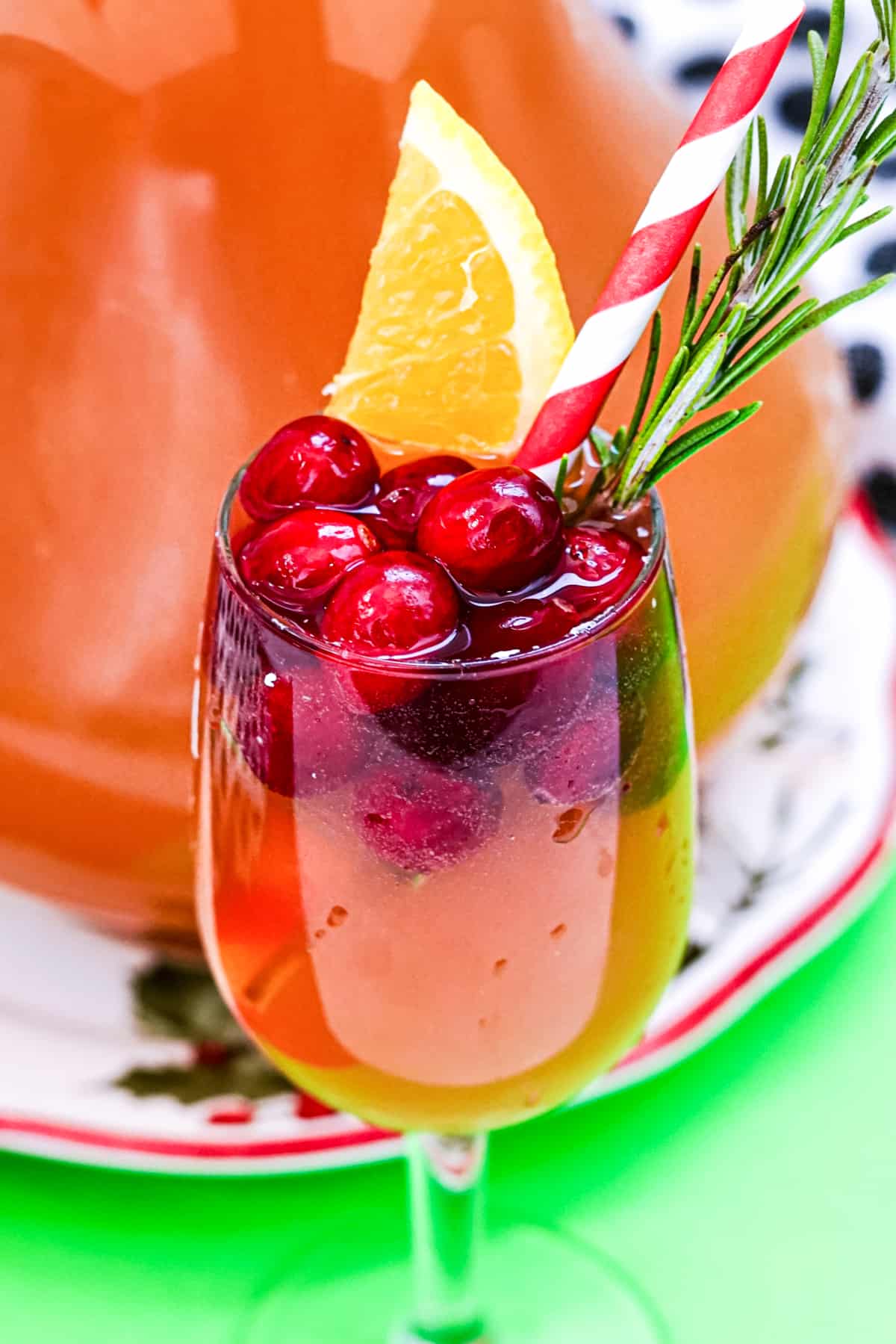 Wine glass with cranberry champagne punch topped with fresh cranberries, orange wedge, sprig of rosemary, and paper straw