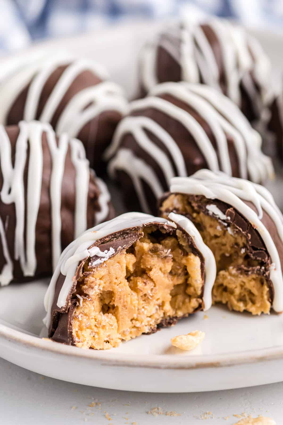 Chocolate Rice Krispie Balls on white plate with one cut in half to show creamy peanut butter and crunchy rice cereal inside.