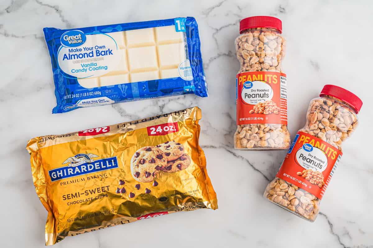 Ingredients for crock pot candy on marble surface, including dry roasted peanuts, semi-sweet chocolate chips, and almond bark.