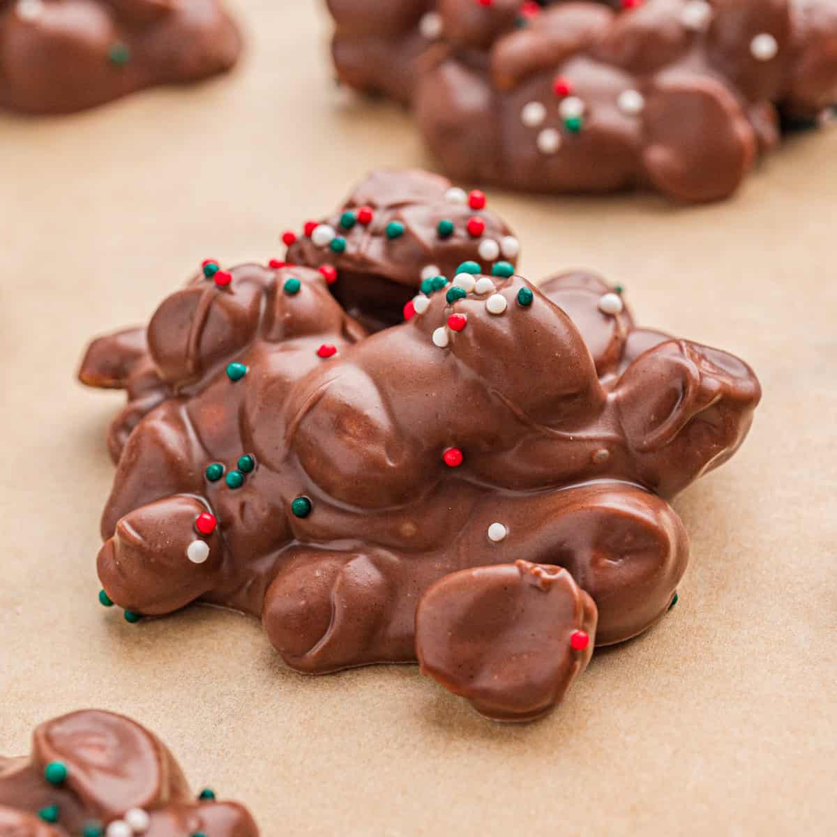 Crock pot candy (aka chocolate peanut clusters) with Christmas sprinkles on parchment paper.