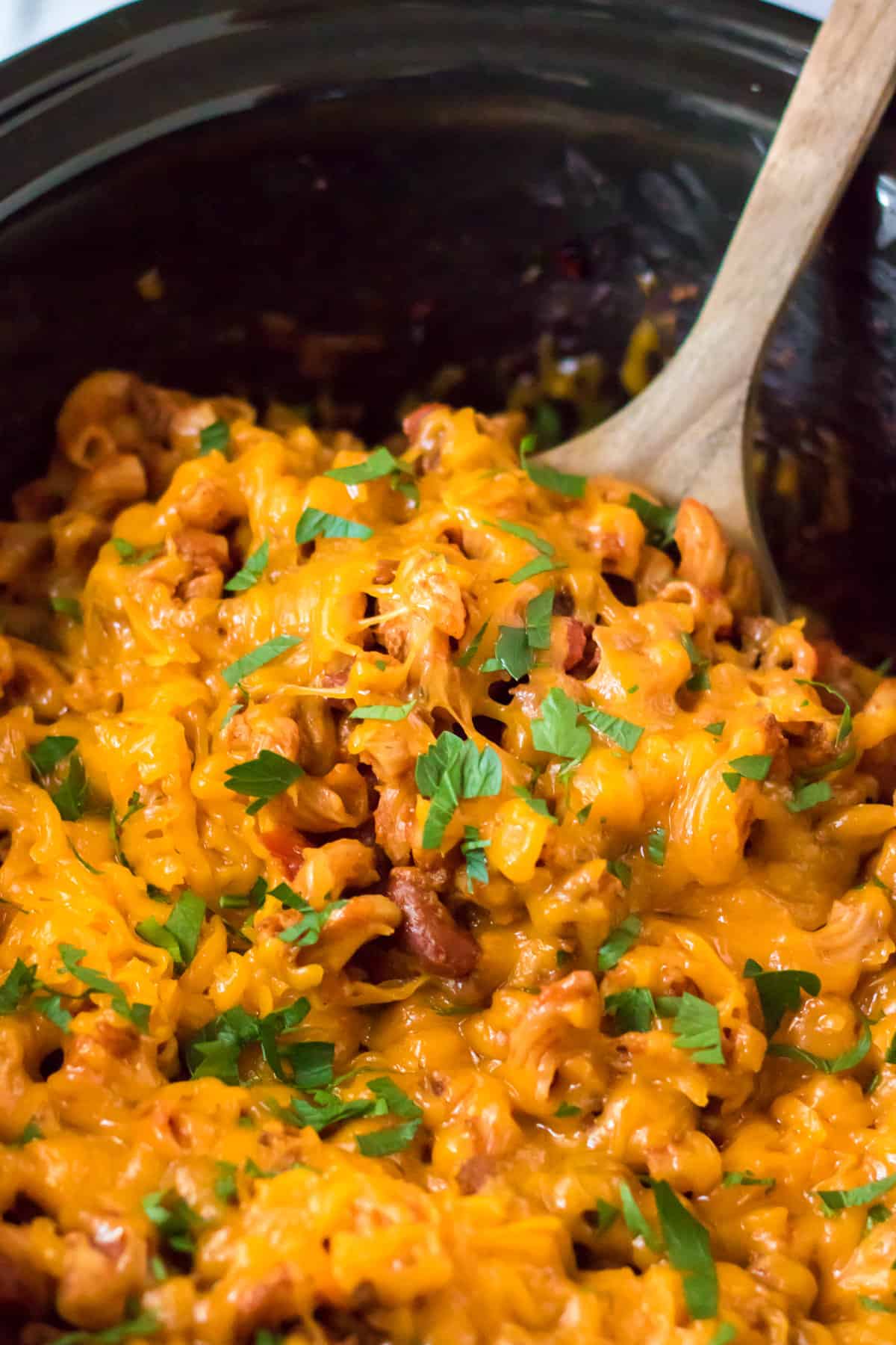 Wooden spoon ground beef chili mac and cheese out of slow cooker.